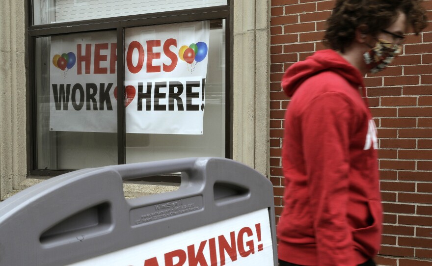 Amid the coronavirus pandemic, a masked pedestrian passes a banner honoring health care workers in the window of a medical center in Boston. House Democrats are proposing hazard pay for front-line workers in a new relief bill.
