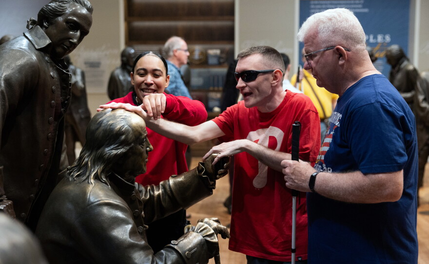 The National Constitution Center in Philadelphia offers guided tactile tours aimed at blind and low vision visitors in a gallery called Signers' Hall. Museum educator Sydney Wharton traces visitor Tim Kelly's Jr. hands over the statue of Benjamin Franklin as she leads him and his father, Tim Kelly Sr., through the gallery.