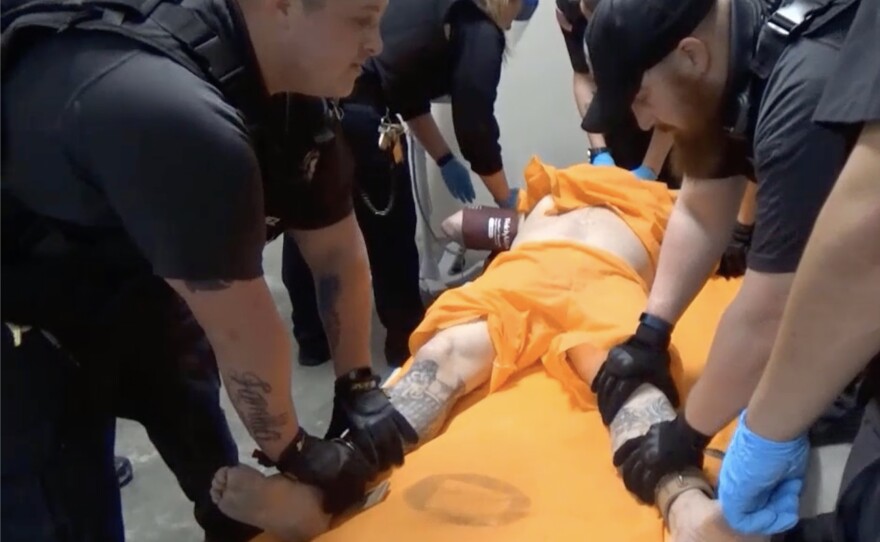 A screenshot from a video of officers at the U.S. penitentiary in Thomson, Ill., holding an incarcerated person in a four-point restraint, where both wrists and ankles are secured to restrict movement.
