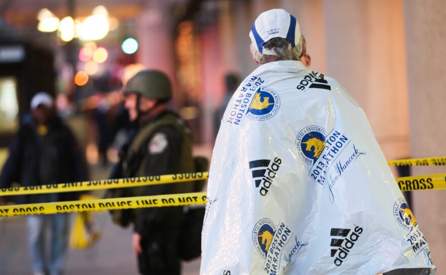 A marathon runner, wrapped in a blanket to stay warm after the race, watched Monday as authorities investigated the bombings that shook the finish line area at the Boston Marathon. At least three people were killed and dozens were wounded.