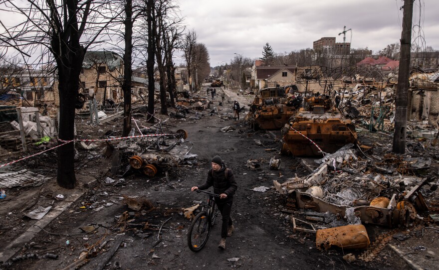 A man pushes his bike through debris and destroyed Russian military vehicles in Bucha, Ukraine, on April 6. The Ukrainian government accused Russian forces of committing a "deliberate massacre" as they occupied and eventually retreated from Bucha, northwest of Kyiv. Hundreds of bodies were found in the days after Ukrainian forces regained control of the town.