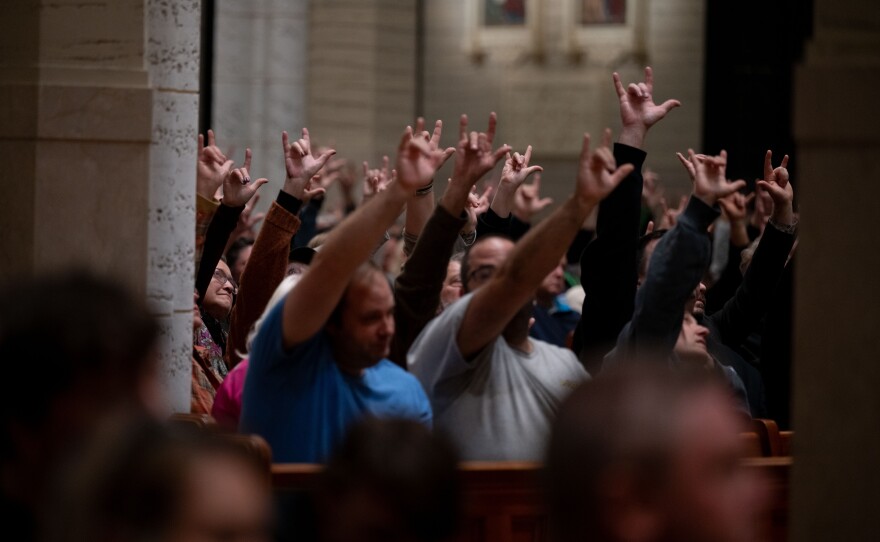 Community memebers sign 'I love you' as Kevin Bohlin, a member of the deaf community, delivers remarks in American Sign Language in the Basilica of Saints Peter and Paul in Lewiston, Maine.