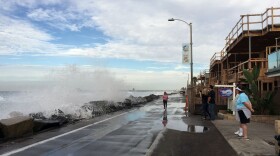 A woman runs at the strand in Oceanside as waves crash against riprap, Oct. 28, 2015.