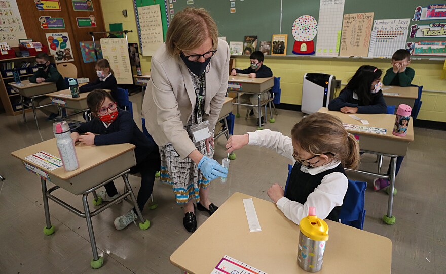 A student gives her coronavirus swab to Helenann Civian, the principal of South Boston Catholic Academy in Boston in January. The White House announced $10 billion to expand testing in K-12 schools.