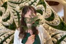 Artist Britton Neubacher poses with her Art Alive rotunda design, "Organized Chaos," during the installation process. She is smiling and holding a preserved plant near her face.