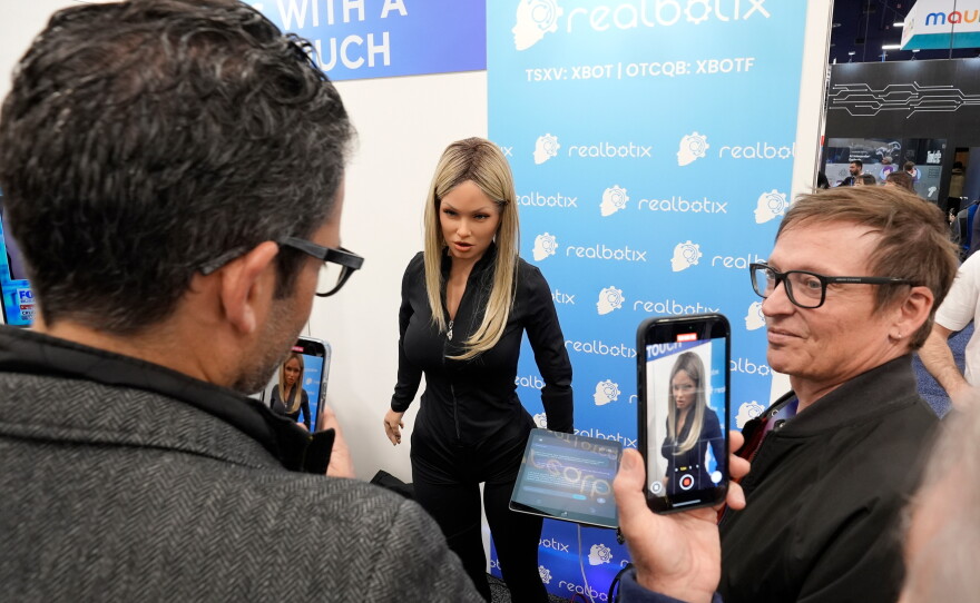 FILE - A Realbotix humanoid robot, center, speaks with attendees at a Realbotix booth during the CES tech show Jan. 8, 2025, in Las Vegas.