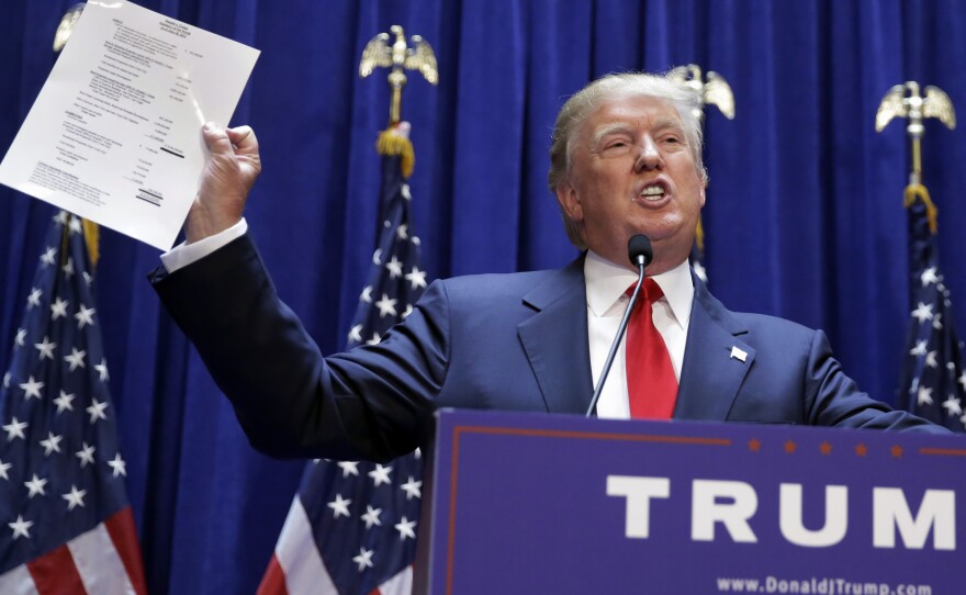 Donald Trump holds up a copy of what he says his net worth is in June 2015. It claims his net worth at almost $9 billion, though others have estimated it to be far lower.