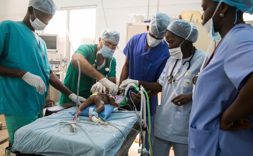Neurosurgeon John Jabang (center, in dark blue scrubs) and his team operate on 2-week-old Biafa Ceesay, who was born with spina bifida. Carlos Fuentes, a physician on loan from Cuba (dressed in green scrubs), is the only anesthesiologist in Gambia. Most anesthesia in the country is administered by nurses.