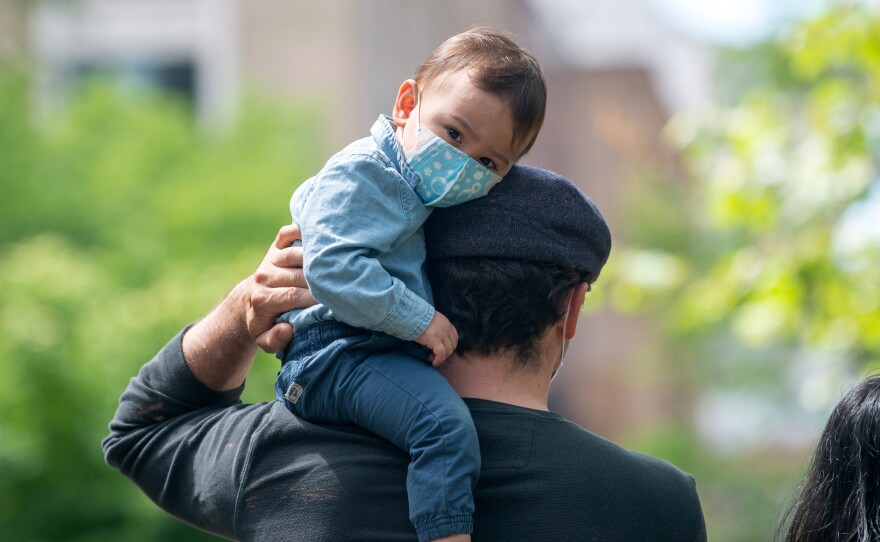 A child wearing a mask sits on his father's shoulder on May 24, 2020, in New York City. Dr. Jose Romero suggests that taking toddlers into the public is a risk.