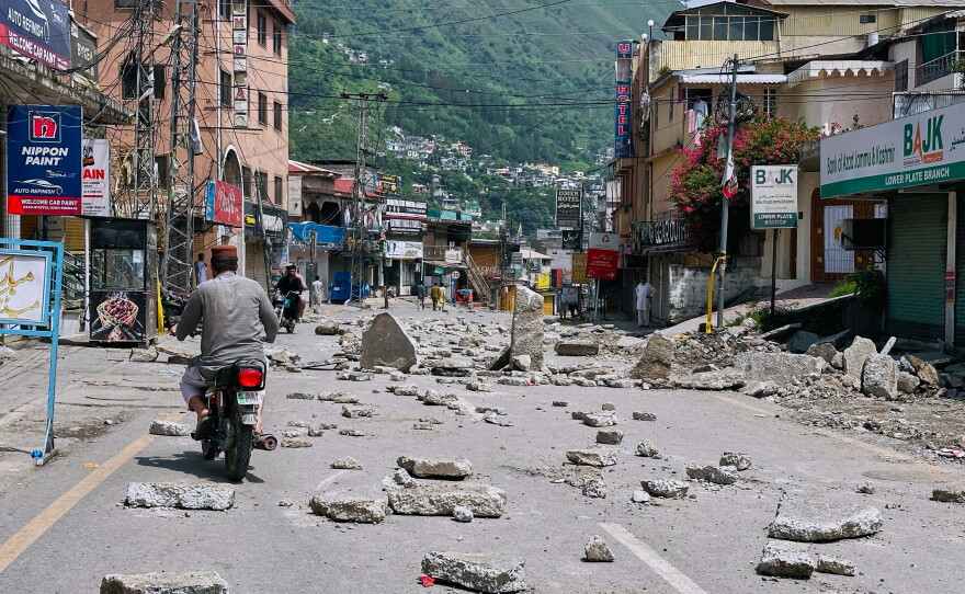 Motorcyclists navigate through a road barricaded with concrete blocks set up by supporters of the outlawed Joint Awami Action Committee (JAAC) during a protest demanding greater political rights and the abolition of 12 legislative refugee seats, in Muzaffarabad, the capital of Pakistan-administered Kashmir, Saturday, Aug. 1, 2026.