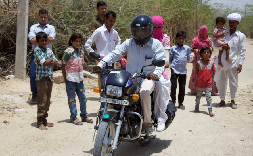 Lumbaram, in white turban holding a child, watches as his brother drives Durga to Jodhpur for her exams.