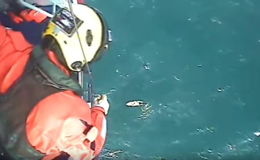 A rescue worker looks down from a helicopter at surfer Matthew Bryce and his board, both battered by a choppy sea.