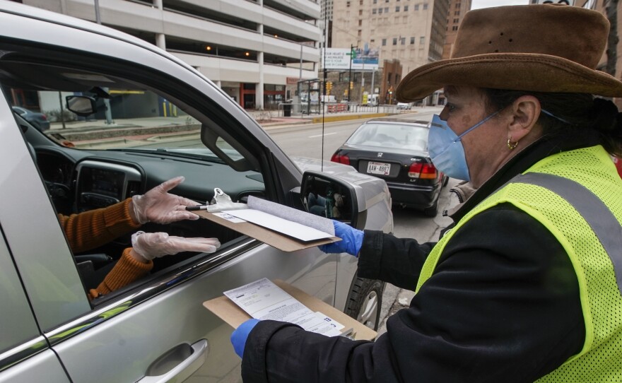Jill Mickelson helps a drive up voter outside the Frank P. Zeidler Municipal Building Monday March 30, 2020, in Milwaukee. The city is now allowing drive up early voting for the state's April 7 election. The state is facing renewed calls to postpone the election amid the coronavirus outbreak.