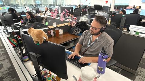 A man at a desk in front of a computer wearing a headset is on the phone with a caller to 211 San Diego.