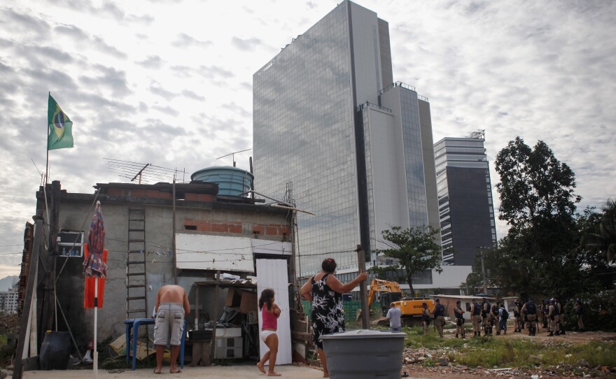 With the Olympics just months away, many wonder whether hosting the Games will be worth the effort. Here, members of the Lopes family watch during the demolition of a building in Rio's Vila Autodromo favela, with new Olympic Park structures in the background, on Feb. 24.