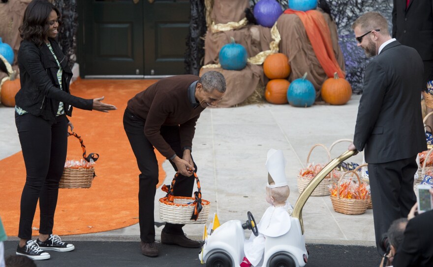 President Barack Obama and First Lady Michelle Obama greet a young child dressed as the Pope and riding in a "Popemobile" as he hands out treats to children trick-or-treating for Halloween on the South Lawn of the White House on Oct. 30, 2015.