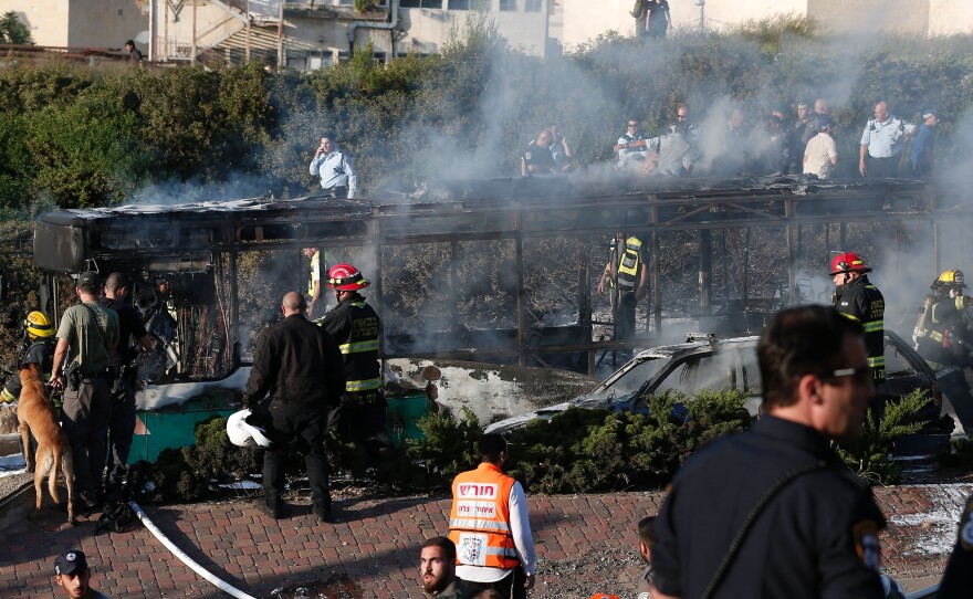 Israeli security forces and emergency services gather around a burned-out bus following the explosion in Jerusalem on Monday.