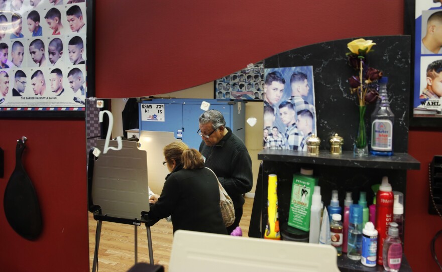 Democratic polling judge John Ramirez (right) is reflected in a mirror as he assists a voter filling out her ballot at Delia's Beauty Salon in Chicago on Tuesday.