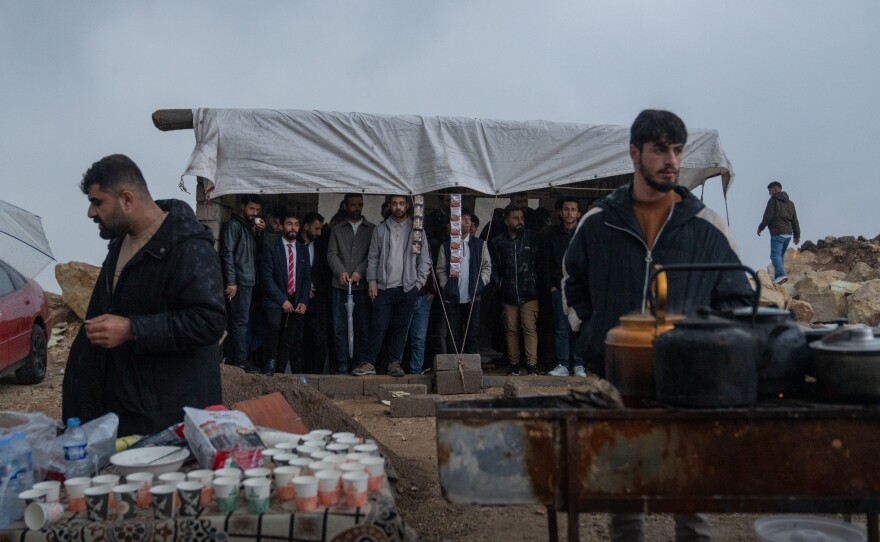 People stand under a tent on a hilltop to avoid the pouring rain while waiting for the Nowruz festivities.