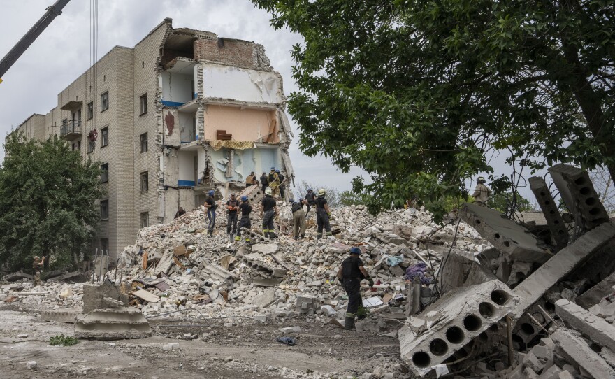 Rescue workers stand on the rubble at the scene of a missile strike that hit a residential apartment block in Chasiv Yar, which is located in Ukraine's Donetsk region. The strike took place Saturday night and left at least 15 people dead.