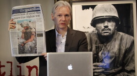 Julian Assange of the WikiLeaks website holds up a copy of The Guardian newspaper as he speaks to reporters in front of a Don McCullin Vietnam war photograph at The Front Line Club on July 26, 2010 in London, England. 