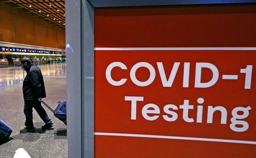 In this file photo, travelers pass a sign for COVID-19 testing at Logan Airport in Boston. The Biden administration is lifting its requirement for COVID testing before flying to the U.S.