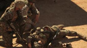 A Marine in Infantry Officers Course uses the radio off a simulated casualty during a patrol at Twentynine Palms

