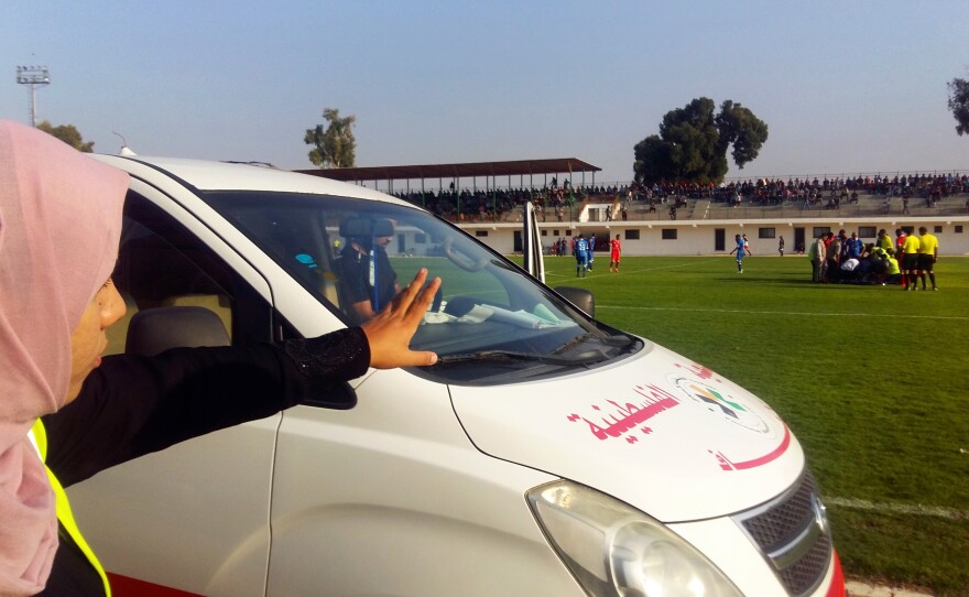 Hanan Abu Qassem motions from the sidelines of a top division professional soccer game in Gaza, poised to treat injured players. Abu Qassem is the first female EMT to staff such games in the Gaza Strip.