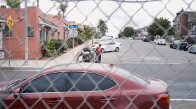 A man transports his belongings in a shopping cart on the city's side of a chain link fence in San Diego on Friday, Aug. 15, 2025.
