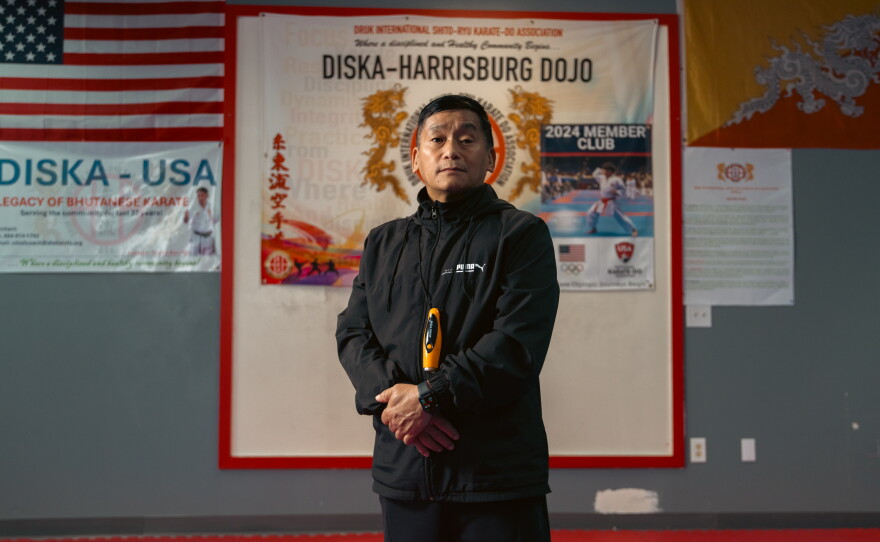 Soke Ran Rai, a martial arts teacher at the DISKA Harrisburg Dojo, began teaching karate in the refugee camps in Nepal before relocating to the United States. He poses for a portrait in the dojo, where the U.S. and Bhutanese flags hang behind him, on April 16, 2025, in Harrisburg, Pa.