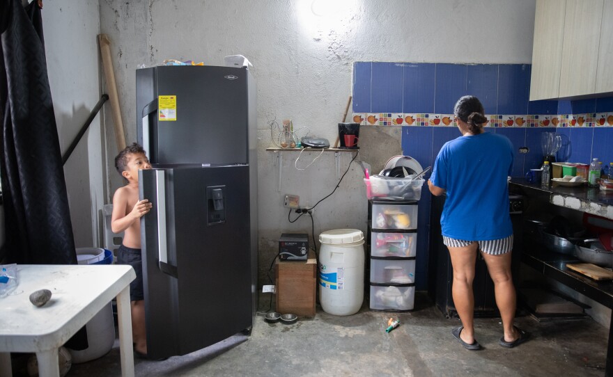 July prepares breakfast for her 6-year-old son, Samuel. She and her husband spend a significant amount of their monthly income to purchase water for drinking. The white container by her side holds water for washing dishes.
