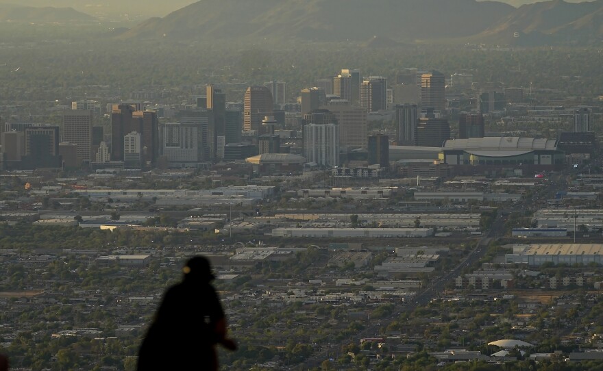 A man overlooks downtown Phoenix at sunset atop South Mountain, Sunday, July 30, 2023. Some slight relief may be on the way as seasonal thunderstorms could drop temperatures in Phoenix on Monday and Tuesday. (AP Photo/Matt York)