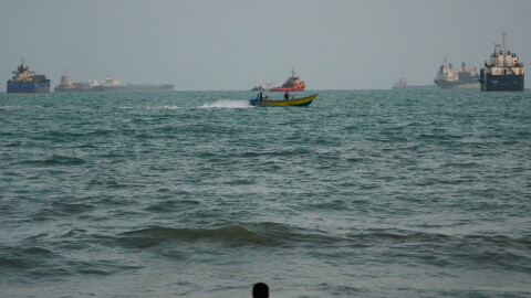 A swimmer remains near the shore as a motorboat passes commercial vessels anchored in the Strait of Hormuz off Bandar Abbas, Iran, on Friday.