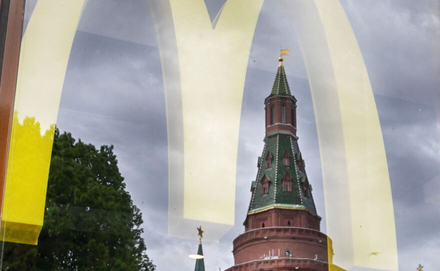 People walk past a window of a McDonald's restaurant as the towers of the Kremlin reflect in it in Moscow on May 26, 2022.