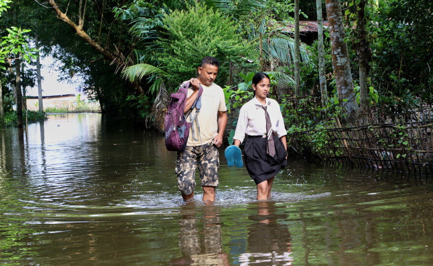 A school girl and her father wade through floodwaters in Alengmora village in Jorhat, India, Monday, Aug. 10, 2026.
