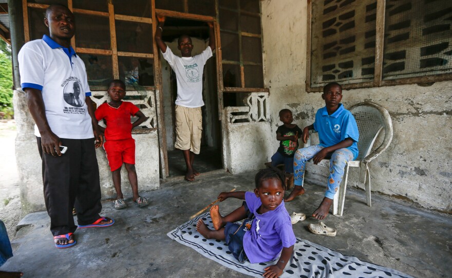 Assistant pastor of the Christ Kingdom Harvest Church, Tarwo Kah, left, stands on the porch of the apartment that his church found for the Kaifa family, who lost their parents to Ebola. The boy in the doorway is Morris Kaifa, 15, and then left to right, Benetta, 4, Antoinette, 2 and Prince, 10.