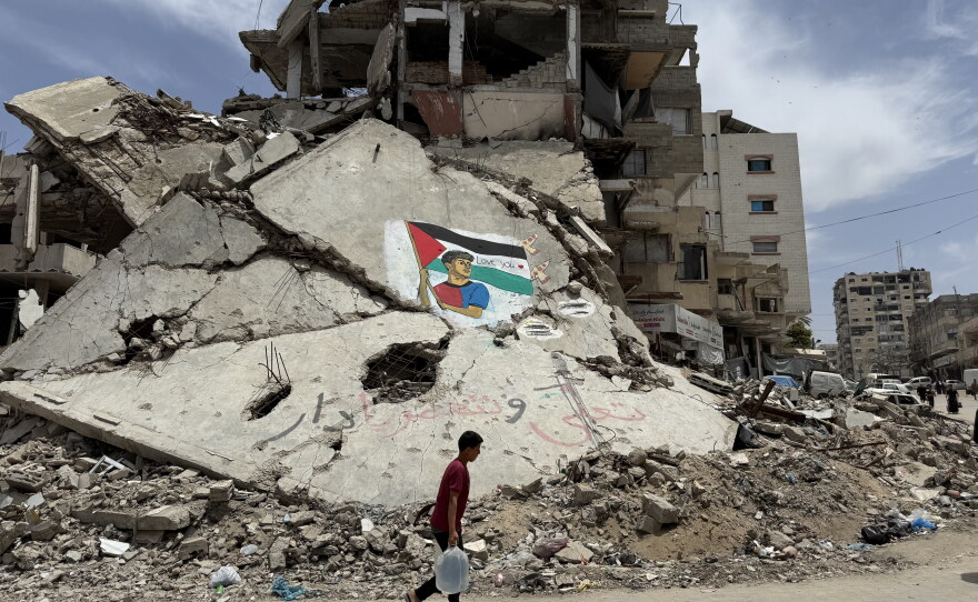 A Palestinian child carries jugs of water as he passes by a mural of Spanish soccer star Lamine Yamal that is painted on the rubble of a home destroyed by Israeli airstrikes, in Al-Shati refugee camp, Gaza, on May 14, 2026.
