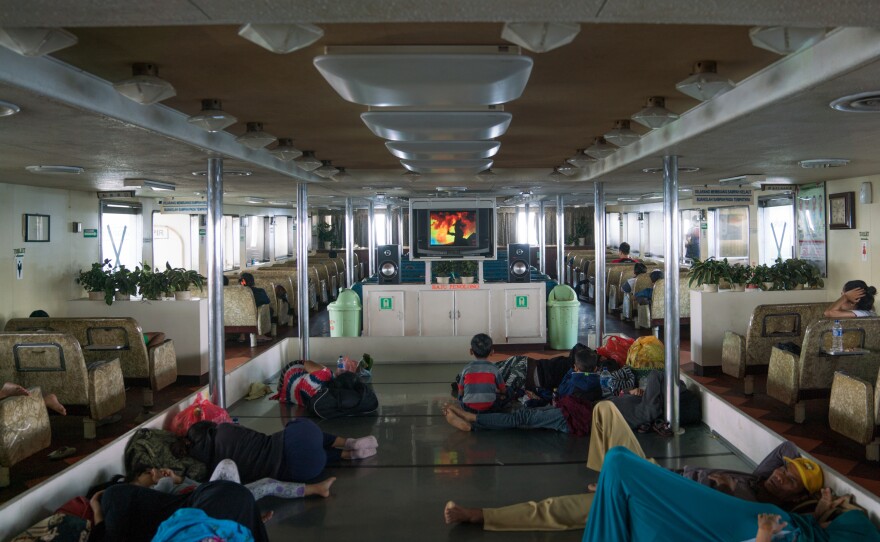 Inside the hold of the ferry, passengers rest while a movie blares on the screen.