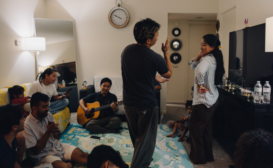 Community members gather for dinner and music at Robin Gurung's home in Harrisburg, Pa., on Sept. 14, 2025. Longtime friends Nawal Rai, who works as a storytelling and communications coordinator for ARU and runs the We Belong Here campaign, and Manju Gurung dance together as everyone sings together and Bibek Rai plays guitar.