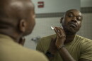 A Black soldier in a green t-shirt looks into a mirror as he shaves his facial hair at Joint Base Lewis-McChord, Wash., Aug. 13, 2026.