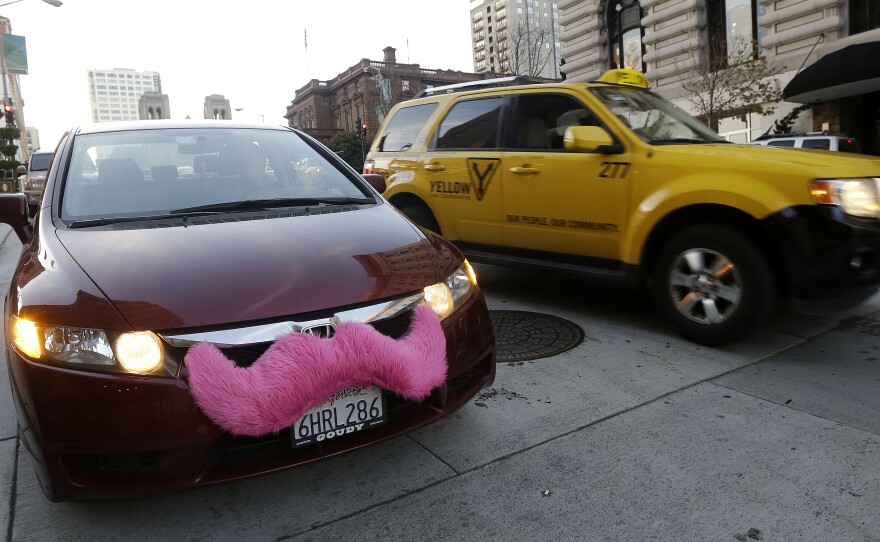 A Lyft driver in San Francisco drops off a passenger as a taxi passes by. The smartphone app lets city dwellers hitch rides from strangers.