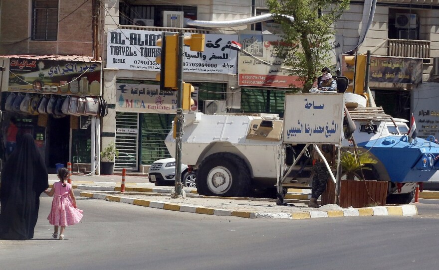 An Iraqi woman and child walk toward an Iraqi security armored personnel carrier on a Baghdad street, a sign of the political showdown between incumbent Prime Minister Nouri al-Maliki and those calling for his tenure to end.