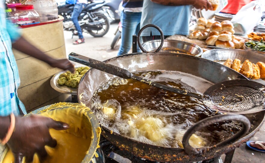 A street vendor frying potato vadas for vada pav in Mumbai's busy Dadar neighborhood.