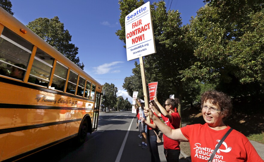 A private school bus passes as West Seattle High School teacher Jennifer Hall pickets with about 50 colleagues outside the school last week. (AP Photo/Elaine Thompson)