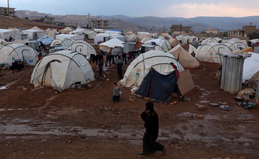 A Syrian refuge woman walks past tents at a refugee camp in the eastern Lebanese border town of Arsal, Lebanon, Monday, Nov. 18, 2013.