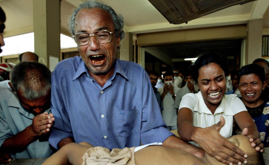 In a Dec. 27, 2004 file photo, a young tsunami victim's father cries as he holds the body of his son along with other family members at the Galle Hospital in Galle, Sri Lanka.