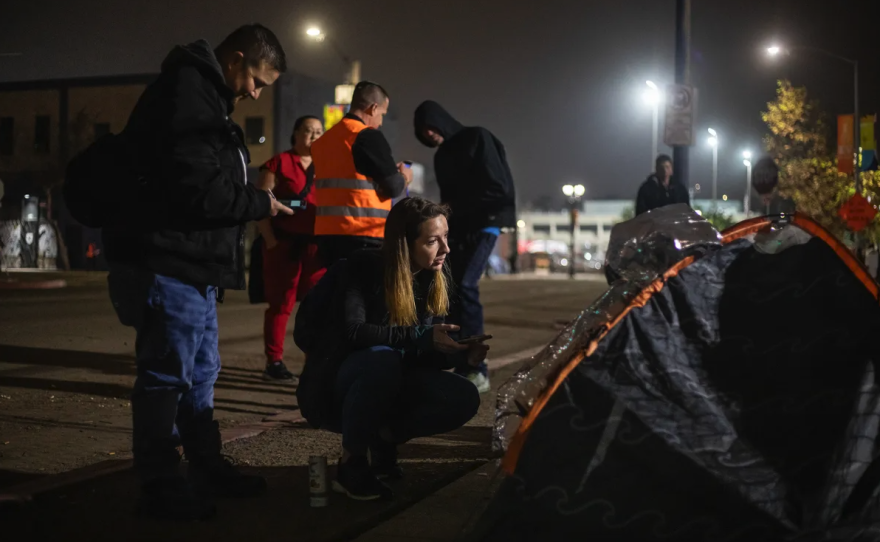 Las voluntarias Michelle Lefever, a la izquierda, y Maggie DuRocher, al centro, encuestaron a un residente sin hogar, para el recuento anual puntual en San Diego el 25 de enero de 2024. La encuesta voluntaria es un requisito obligatorio a nivel federal para recopilar datos sobre la población sin hogar de la región. Foto de Adriana Heldiz, CalMatters