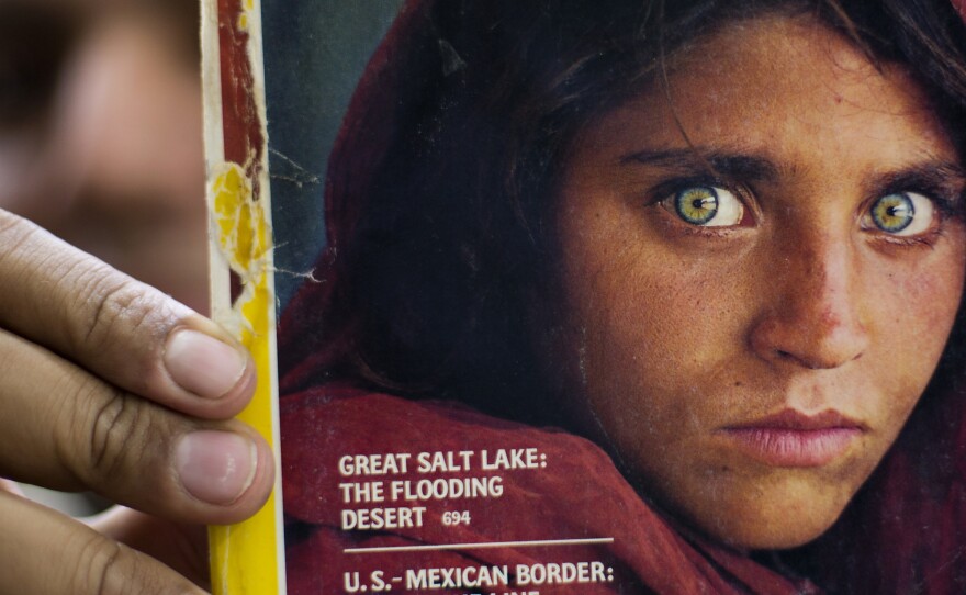 The owner of a bookstore shows a copy of National Geographic magazine with the photograph of Sharbat Gula, when she was around 12 years old.