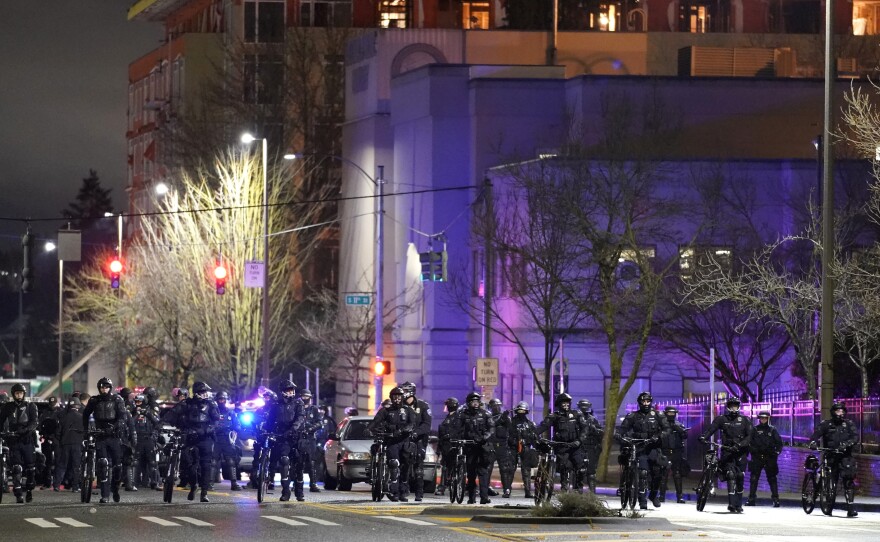 Police and other law enforcement officials stand in a line as protesters approach in the street in front of the City-County Building on Sunday in Tacoma, Wash.