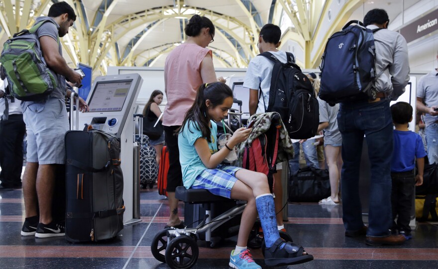 Alisha Lalani, 10, of Ft. Lauderdale, Fla., looks at her phone as her mother and brother check in for their flight to Miami at Washington's Reagan National Airport. Their flight was one of thousands delayed as a result of a technical glitch with an FAA automated system.